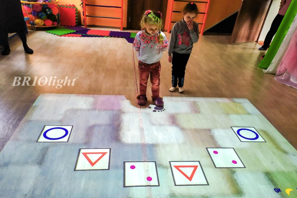 Two girls work with geometric shapes on a Briolight interactive projection